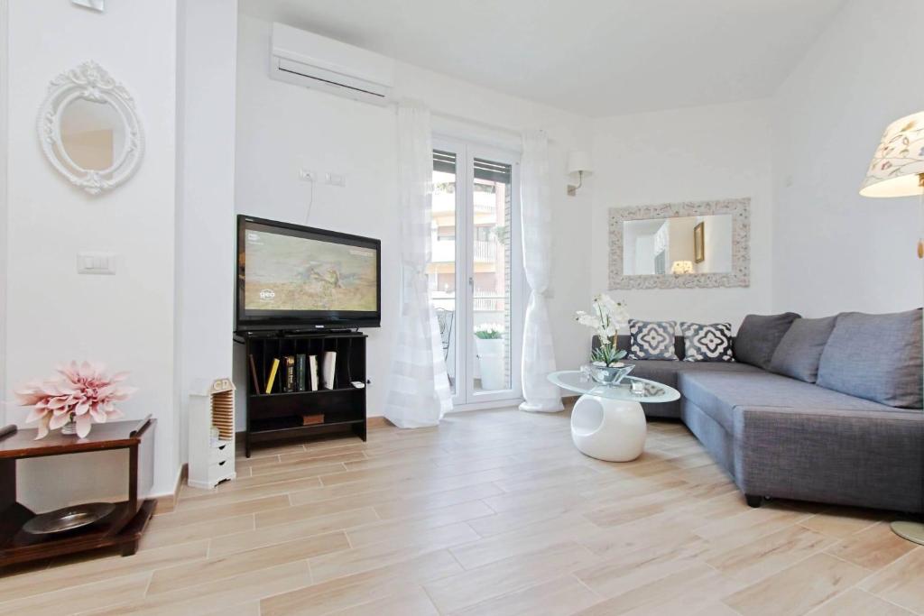 Living room with gray sofa, TV, white walls, wooden floor